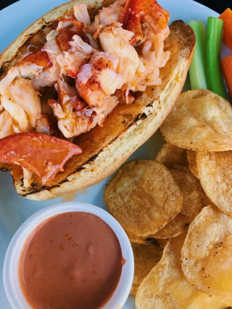 A lobster sandwich with potato chips and dipping sauce.